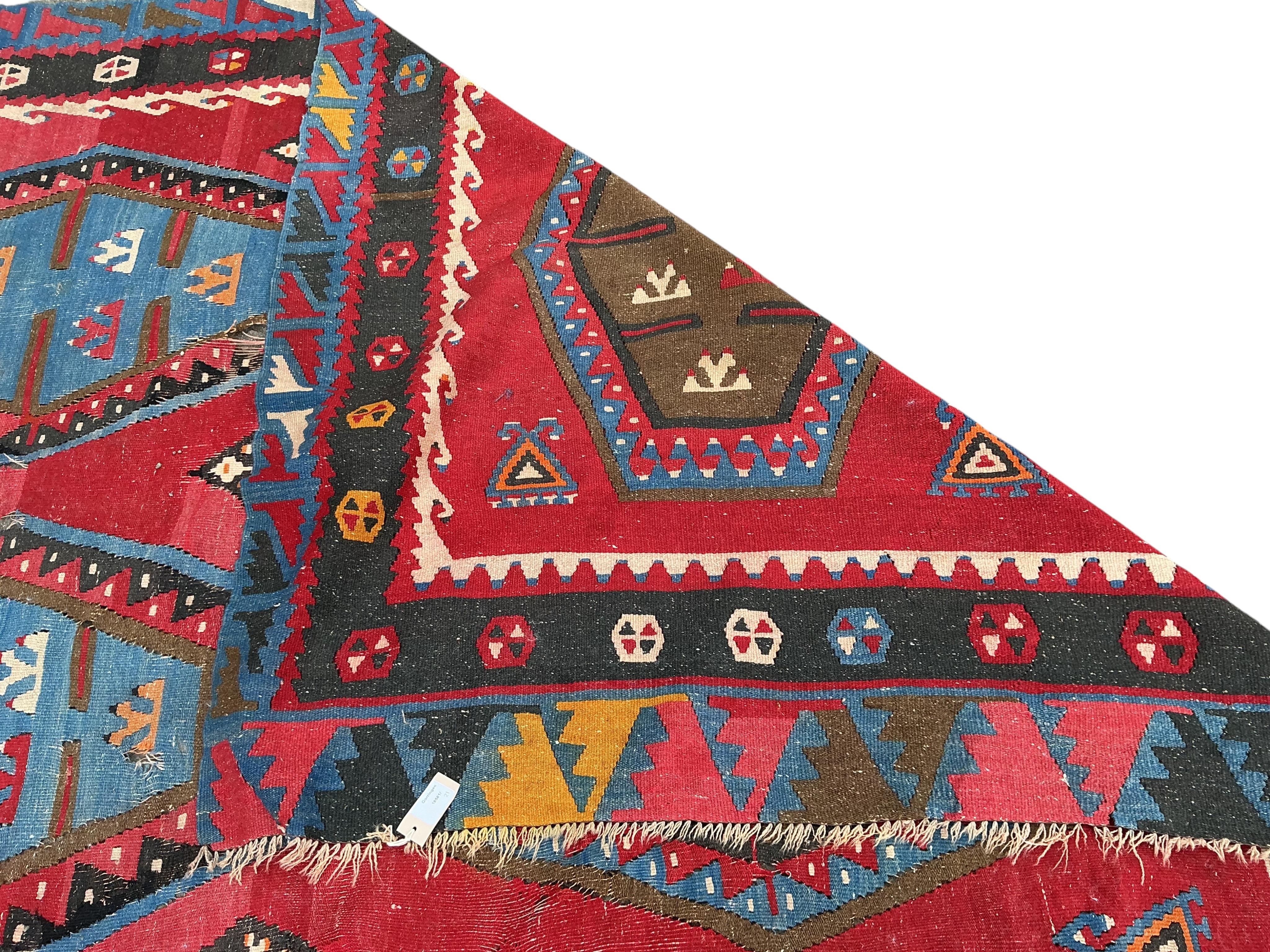 A Turkish Kilim flatweave polychrome carpet, woven with three rows of hexagons, on a red ground, (severely holed and damaged in places), 373 x 267cm